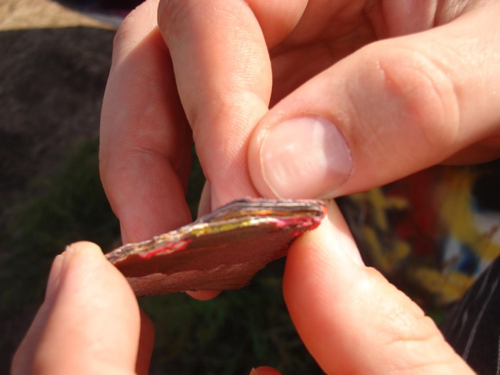Layers of spray-paint are melded together and held between the fingers of an unidentified person.